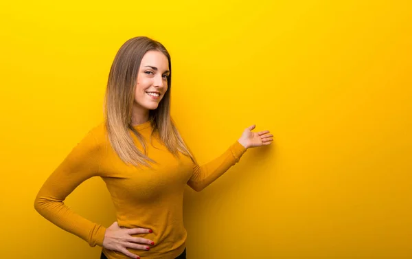 背面を指すと製品を提示背景が黄色の若い女性 — ストック写真
