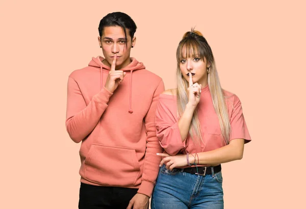 Young couple showing a sign of silence gesture putting finger in mouth over pink background