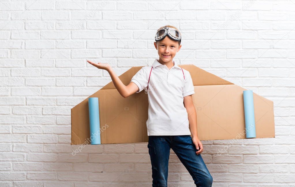 Boy playing with cardboard airplane wings on his back holding copyspace imaginary on the palm