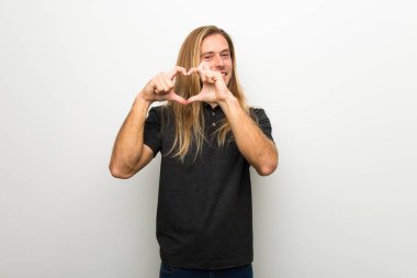Beyaz duvar eller tarafından kalp sembolü yapma üzerinde uzun saçlı sarışın adam