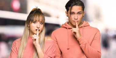 Şehirde parmağını ağzına alan sessizlik jesti gösteren genç çift