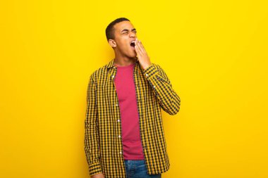 Esneme ve el ile geniş açık ağız kapsayan Sarı zemin üzerine genç afro Amerikalı adam