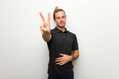 Gülümseyen ve zafer işaret gösteren beyaz duvarın üzerinden uzun saçlı sarışın adam