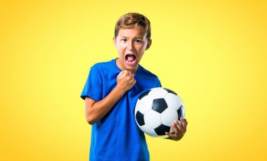 Şanslı çocuk futbol sarı arka plan üzerinde oynamak