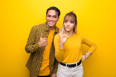Canlı sarı arka plan üzerinde genç çift ok işareti gösteren ve jest kadar bir başparmak veren