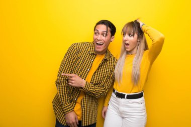 Canlı sarı arka plan üzerinde genç çift yan parmak işaret ve bir ürün sunan