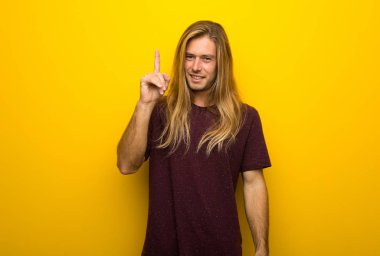 Gösteren ve en iyi iz içinde parmak kaldırma sarı duvarın üzerinden uzun saçlı sarışın adam