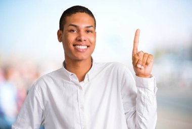 Genç Afro-Amerikan adam gösterilen ve odaklanmamış açık arka plan üzerinde en iyi işareti parmak kaldırma