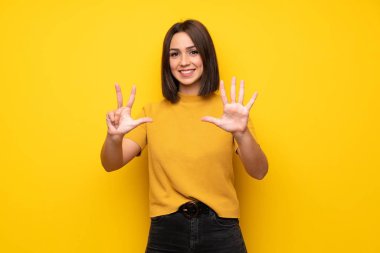 Genç kadın sarı duvar sekiz parmak ile sayma