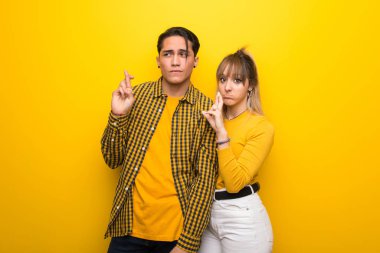 Parmakları geçiş ve en iyi dilek ile canlı sarı arka plan üzerinde Genç çift