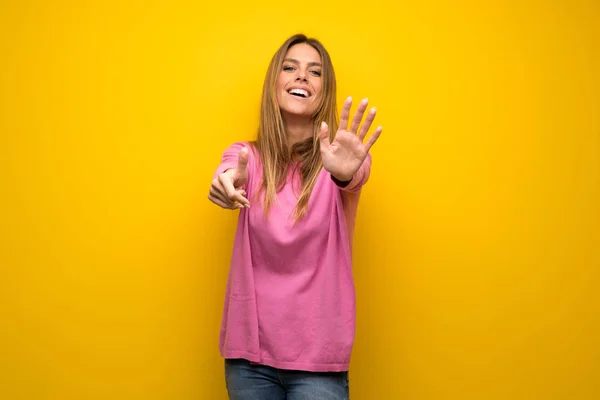 本の指で数える黄色の壁にピンクのセーターの女性 — ストック写真