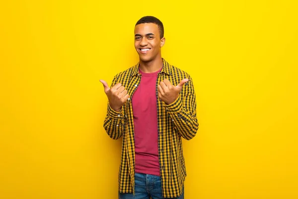 両手でジェスチャーを親指を与えると笑顔の黄色背景に若いアフロ アメリカ人 — ストック写真