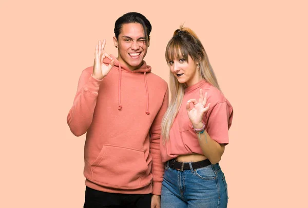 ピンクの背景の上に指でOkサインを示す若いカップル — ストック写真
