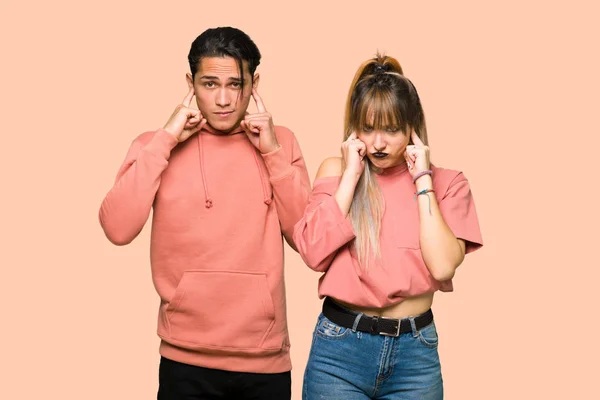 年轻夫妇覆盖两只耳朵与手在粉红色背景 — 图库照片