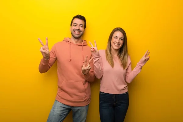 Group of two people on yellow background smiling and showing victory sign with both hands