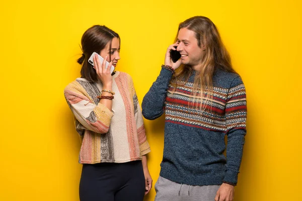 黄色背景的嬉皮士夫妇与手机进行对话 — 图库照片
