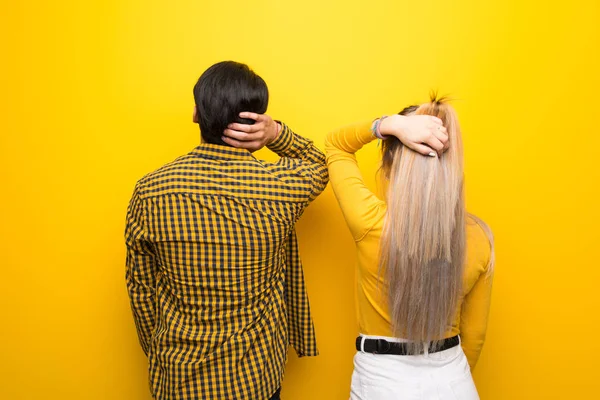 背中の位置に鮮やかな黄色の背景の上に若いカップルは 頭を引っ掻きながら振り返る — ストック写真