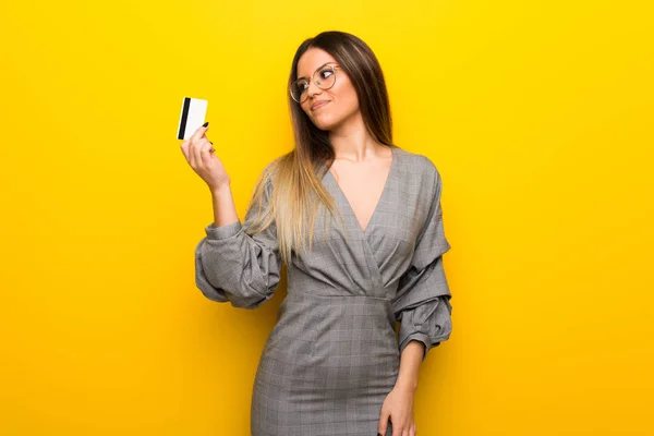 Mujer Joven Con Gafas Sobre Pared Amarilla Sosteniendo Una Tarjeta —  Fotos de Stock