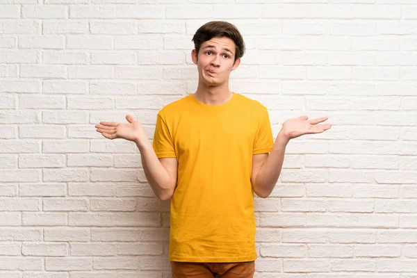 Teenager Mann Über Weiße Backsteinmauer Mit Zweifeln Beim Händeheben — Stockfoto