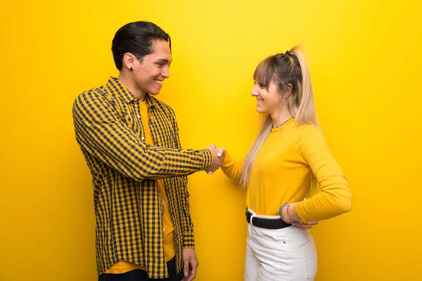 活気に満ちた黄色の背景の上の若いカップルは 良い取引の後に握手 — ストック写真