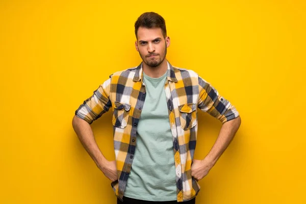 Handsome man over yellow wall angry
