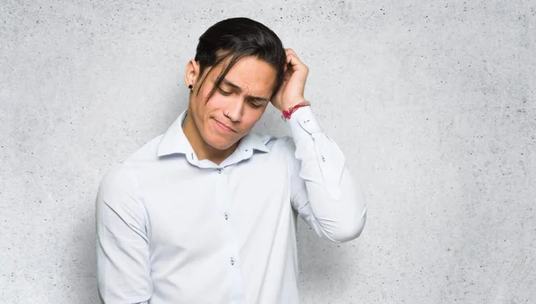 Handsome man having doubts while scratching head on textured wall background