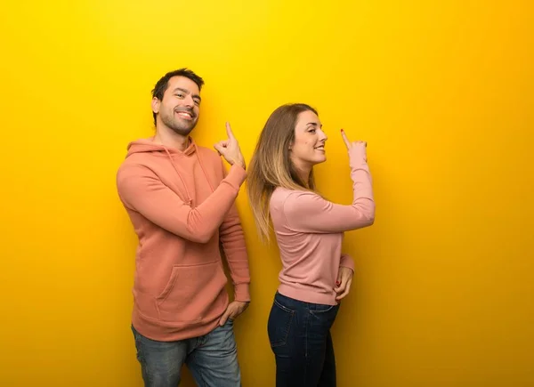 Group of two people on yellow background pointing back with the index finger