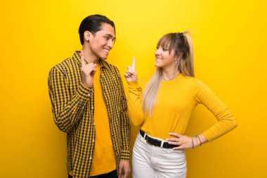 Canlı sarı arka plan üzerinde genç çift gösteren ve en iyi işareti bir parmak kaldırma