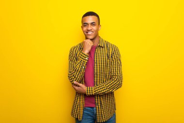 Gülümseyen ve öne doğru emin yüz ile seyir Sarı zemin üzerine genç afro Amerikalı adam