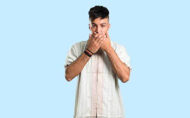 Tipik Arap kıyafetleri giyen Arap genç adam mavi arka planda elleri olan ağzını kapatıyor.