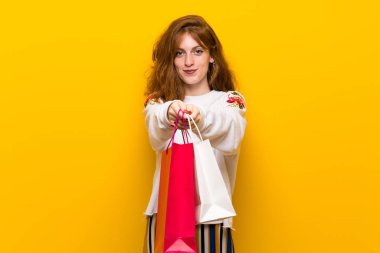 Sarı duvar alışveriş torbaları bir sürü tutan genç Kızıl saçlı kadın