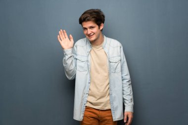 Jean ceket gri duvar mutlu ifade ile el ile selamlayan üzerinde olan genç adam