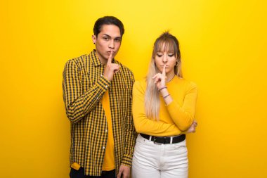 Canlı sarı arka plan üzerinde genç çift ağıza parmak koyarak sessizlik jest bir işareti gösteren