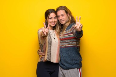 Hippi çift gülümseyen ve zafer işaret gösteren sarı arka plan üzerinde