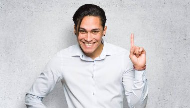 Yakışıklı adam gösteren ve dokulu duvar arka plan üzerinde en iyi işareti bir parmak kaldırma