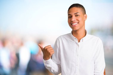 Bakarken bir ürün ya da bir fikir sunmak için genç Afro-Amerikan adam beyaz gömlek bir parmak yanında işaret ile ileri odaklanmamış açık arka plan üzerinde gülümseyen