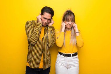 Canlı sarı arka plan üzerinde genç çift elleri ile kulakları kapsayan. Sinirli ifade