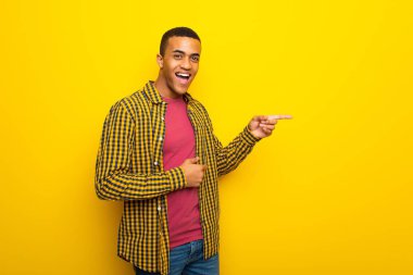 Genç afro Amerikalı adam sarı arka plan lateral pozisyonda yanına işaret parmağı