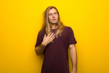 Şaşırttı ve doğru bakarken şok sarı duvarın üzerinden uzun saçlı sarışın adam