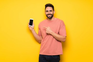 Yakışıklı adam sarı duvar mutlu ve işaret belgili tanımlık hareket eden