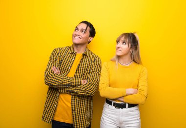 Canlı sarı arka plan üzerinde genç çift gülümseyerek yukarı bakıyor
