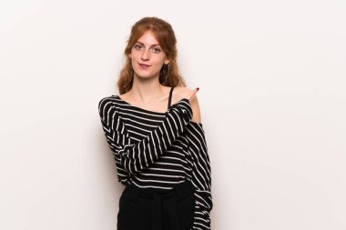 Beyaz duvar tarafına işaret eden bir ürün sunmak için genç Kızıl saçlı kadın