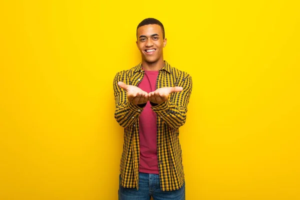 アメリカの若いアフロ男手のひらに架空 Copyspace を保持している黄色の背景に広告を挿入するには — ストック写真