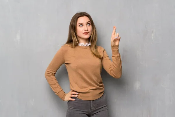Teenager girl over textured wall with fingers crossing and wishing the best