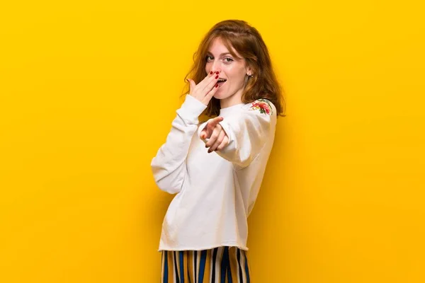 Молода Руда Жінка Над Жовтою Стіною Вказує Пальцем Когось Сміється — стокове фото