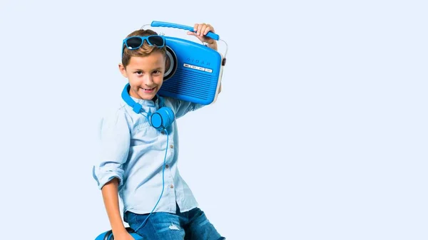 带着太阳镜和耳机的男孩拿着蓝色背景的收音机带着手提箱旅行 — 图库照片