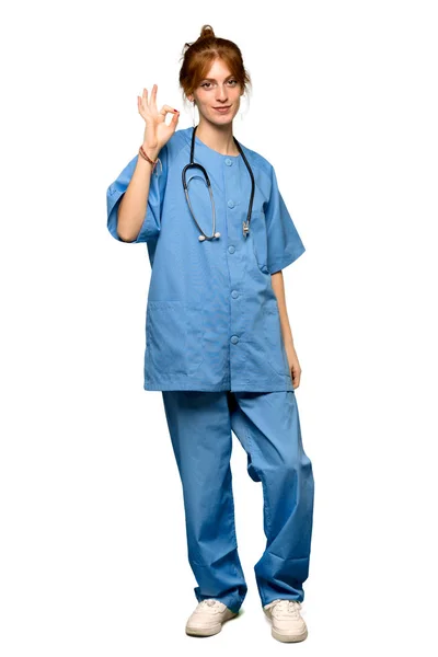 分離の白い背景の上の指で サインを示す赤毛の若い看護師のフルレングス ショット — ストック写真
