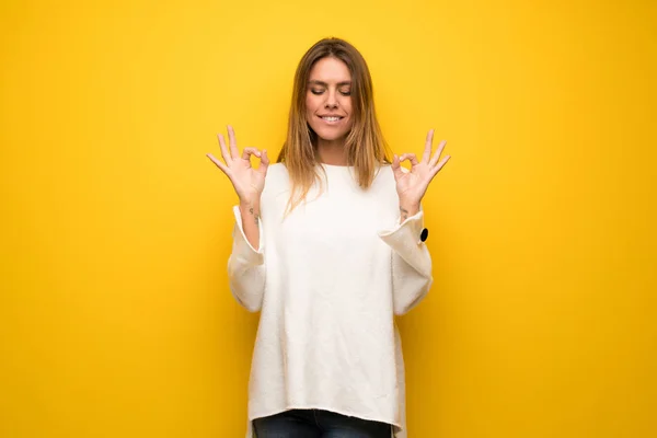 Blonde woman over yellow wall in zen pose