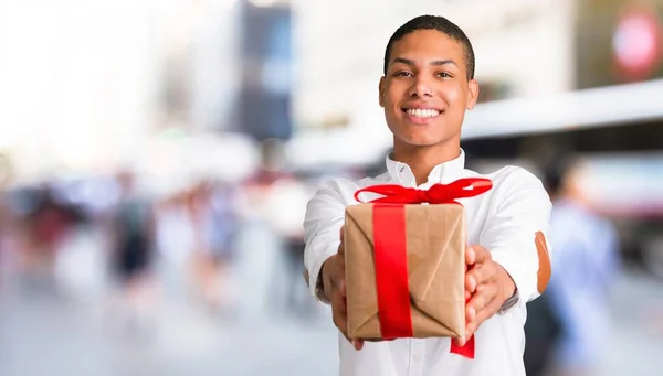 年轻的非洲裔美国人男子与白色衬衫持有礼品盒在手在城市中部 — 图库照片