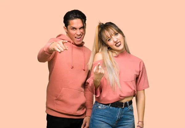 Young couple frustrated by a bad situation and pointing to the front over pink background